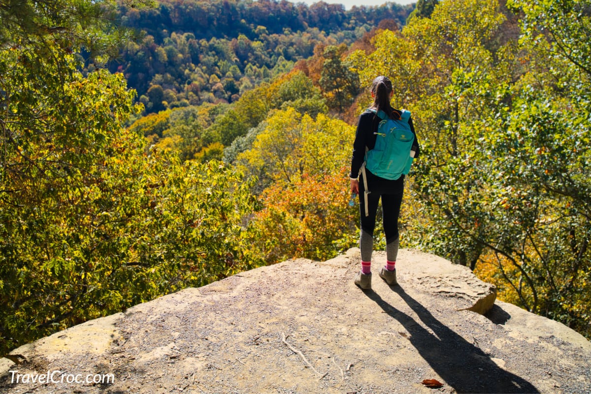 Lady standing on edge of cliff with colorful fall colors in background