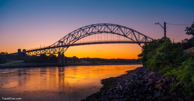 Cape Cod in October Weather - Sagamore Bridge Sunrise over Cape Cod Canal. Dawn Silhouette Architectural Image with Orange and Golden Colors. High Contrast Panoramic Seascape Image with Space for Text and Design.