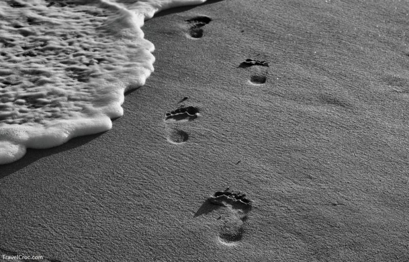 Line of footprints on the beach with wave foam line