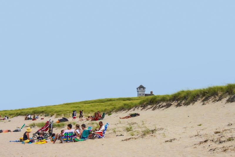  Cape Cod in August - Provincetown Cape Cod USA - Sun worshipers at the beach at National Seashore some on becach chairs and some on sand with dunes and lighthouse behind