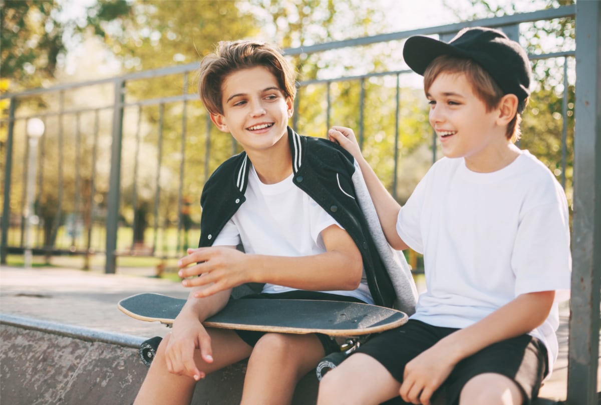Teenagers sit in a skatepark, relax after skateboarding and chat.