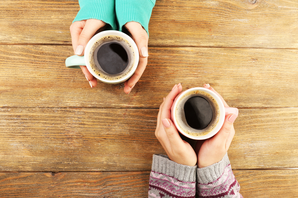 Two pairs of hands holding cups of coffee.